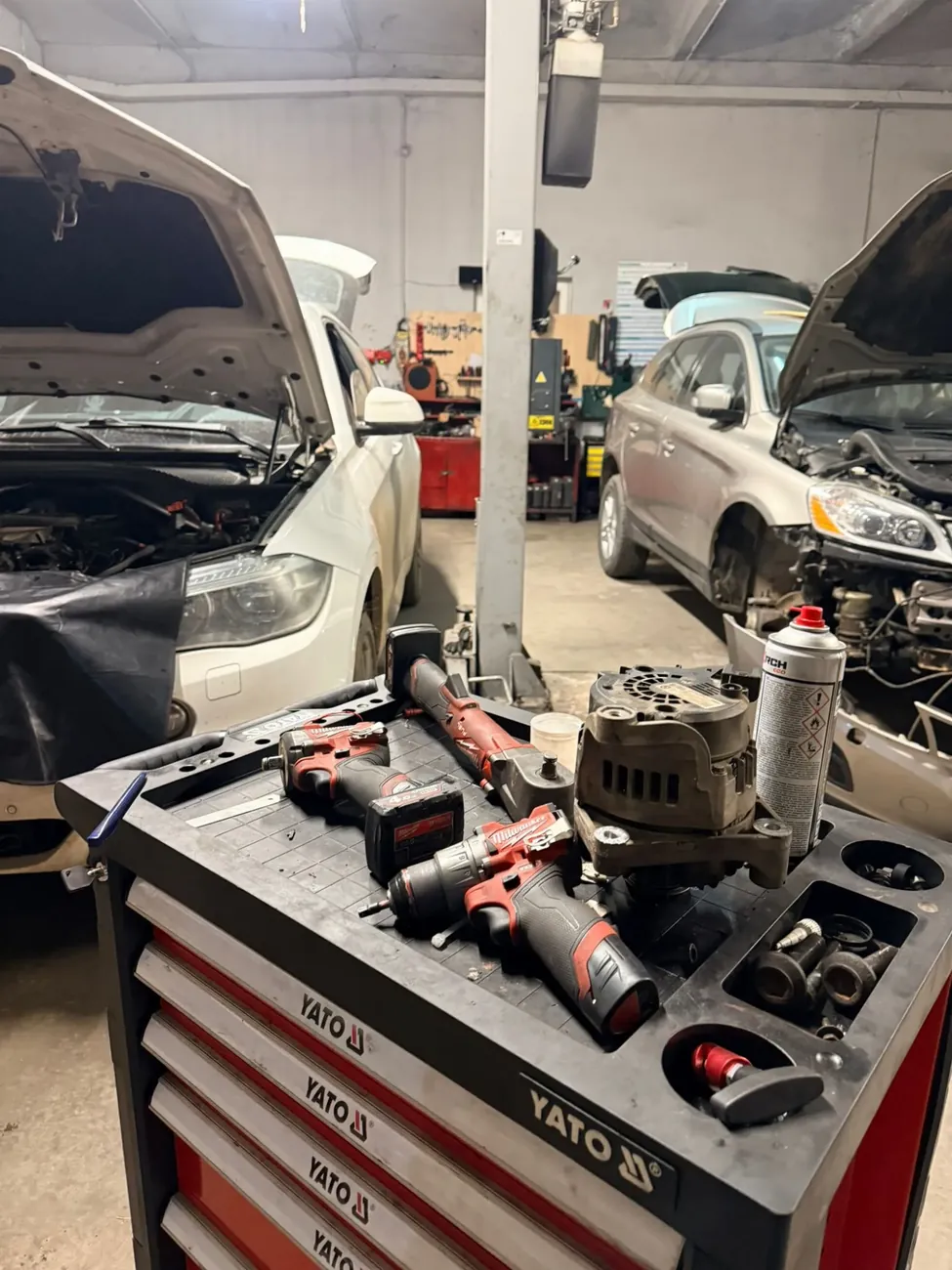 Cărucior cu scule și un alternator demontat, între două mașini cu capota ridicată în atelierul Benjamin Fix Service din Dumbrăvița, la marginea de nord a Timișoarei